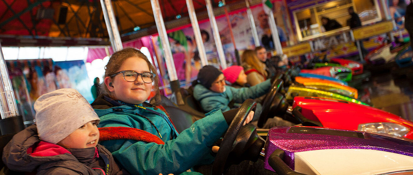 Mehrere Kinder mit Jacken und Mützen sitzen in Autoscootern.